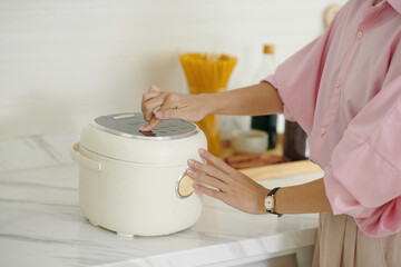 Close-up of woman pushing button to turn on the multicooker during her cooking in the kitchen