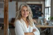 © Nognapas - Portrait of 50 years old smiling woman looking at camera with crossed arms. Happy girl standing in creative office. Successful businesswoman standing in office with copy space.