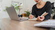 © wichayada - Woman Working from Home in Modern Setting with Laptop and Notebook, Remote Work Concept