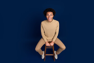 Sticker - Full length photo high view of handsome young man sit chair smile dressed stylish beige garment isolated on dark blue color background