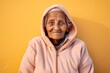 © Markus Schröder - Portrait of a tender indian elderly woman in her 90s wearing a zip-up fleece hoodie on solid pastel color wall