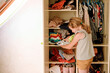 © Irina Schmidt - Little school girl standing by wardrobe with clothes. Preschool child putting shirts away and making decision for shirt to wear. Children get dressed in the morning for school.