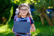 © Irina Schmidt - Happy little kid girl with eye glasses with backpack or satchel and big school bag on the first day of school. Healthy adorable child outdoors. Child holding chalks desk for first schoolday.