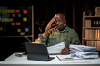 © Wasana - A man is sitting at a desk with a laptop and piles of papers