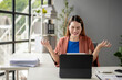 © Wasana - A woman is sitting at a desk with a laptop and a stack of papers