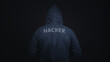© TimmyTimTim - A man is wearing a hoodie with the word hacker on it. The image has a dark mood and a sense of mystery. Cybersecurity concept.