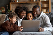 © Peeradontax - A joyful African American family sitting together on a cozy sofa in their living room, sharing a moment of laughter and connection while looking at a laptop.