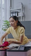 Wall Mural - Young woman carefully packs clothes into a suitcase for an upcoming trip. Natural light illuminates the household scene as she prepares methodically in slow motion