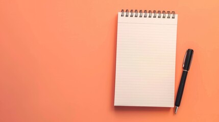 View from above of a notepad and pen on a peach colored surface Educational concepts with blank notebook page