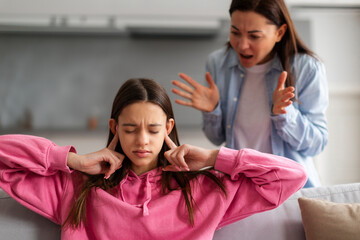 Family problems. Offended teen girl covering ears, not wanting to listen to her mother's scolding, woman having fight with her daughter, quarrelling at home