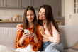 © Home-stock - Happy European family mom with teen daughter using cellphone together at home, watching social media videos, doing online shopping, sitting on sofa together
