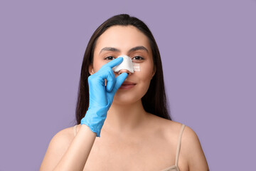 Sticker - Plastic surgeon's hand and young woman with bandaged nose on lilac background