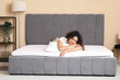 © Pixel-Shot - Happy young African-American woman with pillow lying on soft mattress in bedroom