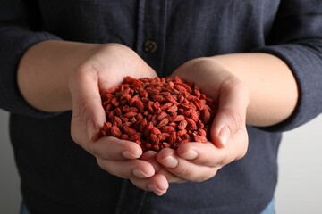 Wall Mural - Woman holding pile of dried goji berries on light background, closeup