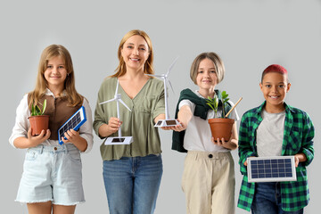 Canvas Print - Pupils with teacher holding wind turbine models and portable solar panels on light background. Ecology concept