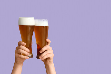 Hands with glasses of beer on lilac background