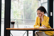 © Satori Studio - A young woman in a yellow blazer works on her laptop in a bright, modern office with large windows and natural light.