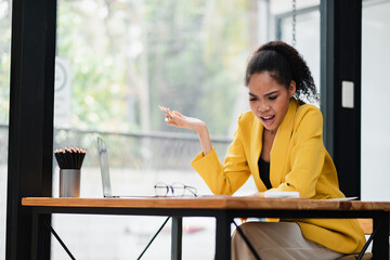 Wall Mural - A young businesswoman in a yellow blazer showing frustration while working at her desk in a modern office setting.