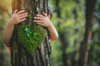 © sornram - A child hugs a tree with a moss heart in a lush forest, symbolizing love and connection to nature.