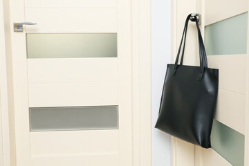 Poster - Black leather bag on door handle on light background, space for text