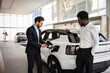 © sofiko14 - Dealer sells electric SUV to businessman in modern car dealership. Business negotiation about environmentally-friendly vehicle. Modern showroom conveys professional atmosphere.