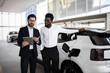 © sofiko14 - Car salesman using tablet to explain features of electric SUV to potential buyer in modern dealership. Business meeting focuses on environmentally friendly transportation and automotive technology
