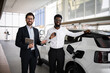 © sofiko14 - Dealer presents new electric SUV to businessman inside modern car dealership. Businessman holds car keys while the vehicle charges. Concept of clean energy, eco-friendly transport, and business.