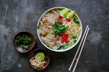 Wall Mural - A Bowl Pho Bo traditional Soup with beef, rice noodles, ginger, lime, chili pepper in bowl. Close up. Vietnamese cuisine served on black background