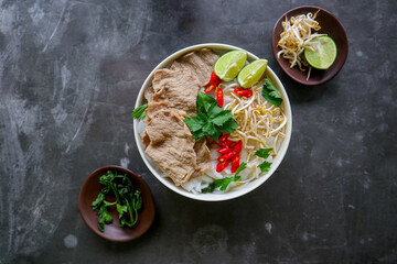 Wall Mural - A Bowl Pho Bo traditional Soup with beef, rice noodles, ginger, lime, chili pepper in bowl. Close up. Vietnamese cuisine served on black background