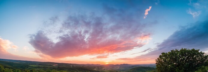 Canvas Print - panoramic view of a sunset over a field of grass. The sky is ablaze with vibrant colors of orange, pink, and purple as the sun dips below the horizon. The field of green grass stretches towards the ho