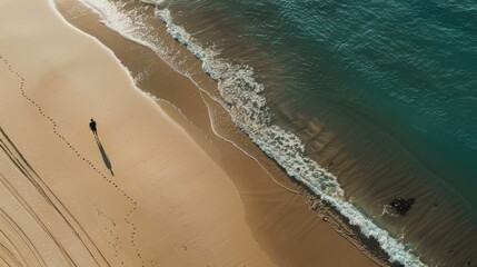 A person walks along the shoreline of the ocean, with waves and sand in the background