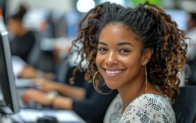 Wall Mural - A woman with curly hair is smiling at the camera. She is sitting at a desk with a computer and a keyboard