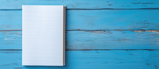 Poster - Looking down on a blue wooden surface, a man's hand holds a blank booklet, creating a minimalist composition with copy space image.