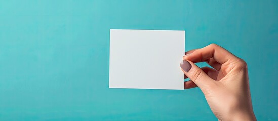 Poster - Close up of a woman's hand holding a blank card against a blue backdrop with copy space image.