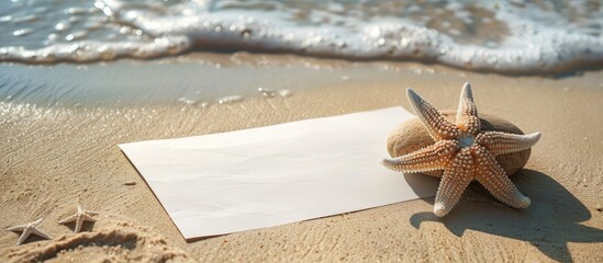 Aufkleber - A blank sheet of paper rests on sandy beach, next to a stone featuring a small seastar, creating a serene scene with copy space image.