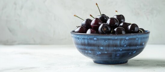 Wall Mural - A blue bowl on a white background filled with fresh ripe black cherries ready for your own image or text. with copy space image. Place for adding text or design