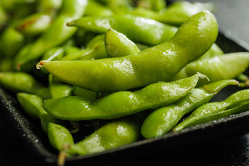 Wall Mural - Green edamame pods. Fresh soybeans on plate on black table.