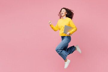 Full body side view young IT woman wear yellow sweatshirt casual clothes jump high hold use work on laptop pc computer isolated on plain pastel light pink background studio portrait Lifestyle concept