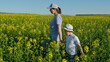 © artifex.orlova - Mom And Son On Yellow Bloomed Rapeseed Field. Woman And Child Walks In Green Rapeseed Field Against Bright Sky. Farming.