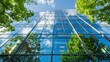 © Lucy - Eco-friendly green building with modern glass facade reflecting blue sky and lush green trees. Sustainable architecture and environmental design concepts for urban offices.