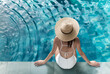 © Kritchanok - woman wearing straw hat and white swimming suit sitting on the edge of pool