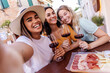 © Xavier Lorenzo - Three multiracial young women taking selfie portrait while drinking red wine gathered on table at restaurant. Food, beverage and friendship concept.