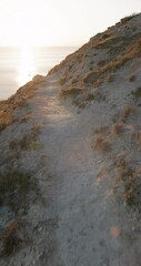 Wall Mural - Walking on path on rocky cliff coastline with sunset warm tones, vertical footage