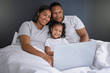 © Lumeez23/peopleimages.com - Happy family, girl and online with laptop in bedroom for chill or unwind on weekend, morning and relax for movies. Mother, father and child in home with internet for streaming, video and cartoon film