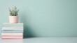 © nattapon98 - Succulent in pink pot on stacked pastel books against a mint green wall. Minimalist decor with negative space.