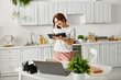© LIGHTFIELD STUDIOS - Middle-aged woman absorbed in reading book while standing in kitchen.