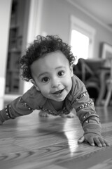 A young child is learning to crawl on a plain background, captured in black and white