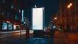 © Fitriyani - Mockup. Blank white vertical advertising poster billboard standing in city at night. Digital screen display light box for advertising or information on modern city street.