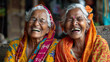 © khonkangrua - Two elderly women in colorful traditional attire share a joyful laugh, showcasing happiness and friendship in a vibrant setting.