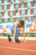 © yavdat - woman in blue sportswear gets into a starting position on a track, ready for a run. This image captures the moment of anticipation and focus before a workout.